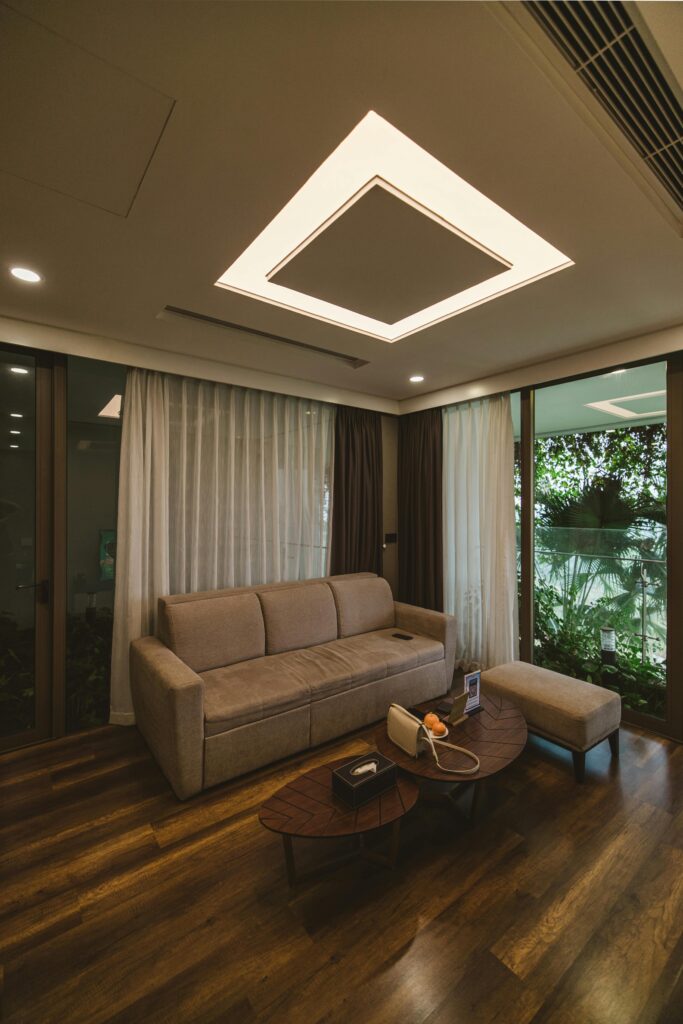 A stylish modern living room featuring a cozy sofa, lush greenery, and natural light from large windows.